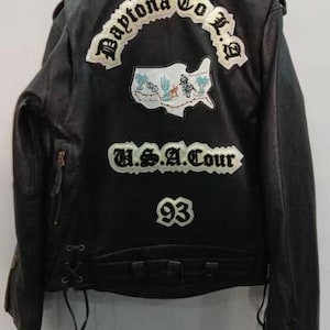 Könnte beinhalten: Schwarze Lederjacke mit gestickten Aufnähern. Auf der Rückseite befinden sich Aufnäher mit den Texten "Daytona To L.A.", "U.S.A. Tour" und der Zahl "93". Eine Karte der USA mit einer Wüstenlandschaft ist ebenfalls vorhanden.