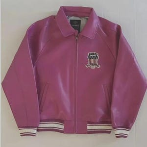 May include: A magenta leather jacket with a zip-up front, collared neckline, and ribbed cuffs and hem with white stripes. An emblem is on the chest. The jacket has two front pockets.