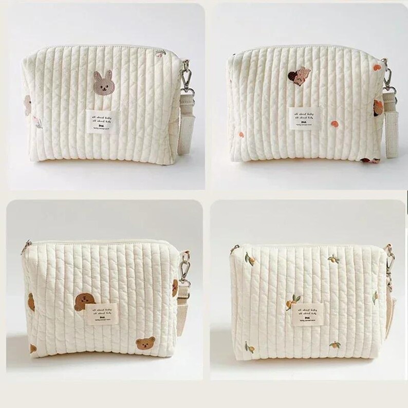 以下が含まれることがあります： クリーム色のキルティングクロスボディバッグ4点。それぞれ異なる刺繍デザインが施されています。各バッグは長方形で、ジッパー開閉、取り外し可能なショルダーストラップ、そして「all about baby」と書かれた小さなラベルが付いています。バッグには動物や花の刺繍が施されています。