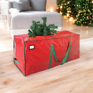 May include: A large red Christmas tree storage bag with green trim and handles. A small green artificial tree is on top of the bag. The bag has a small white label that says "Tree".