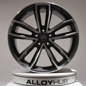 Könnte beinhalten: Eine schwarze und silberne Leichtmetallfelge mit Mehrspeichen-Design. Das Rad hat das Audi-Logo in der Mitte und wird auf einer weißen Plattform präsentiert. Der Text "ALLOYHUB" ist auf der Plattform sichtbar.