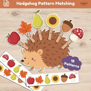 Puede incluir: Un set educativo Hedgehog Pattern Matching que incluye un erizo de cartón marrón, pinzas de madera con iconos de manzana roja, hoja naranja, pera verde, girasol amarillo, bellota marrón y seta roja, junto con tiras de patrones.