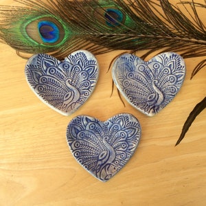 May include: Three heart-shaped ceramic dishes with a blue and white peacock design. The dishes are on a wooden surface.