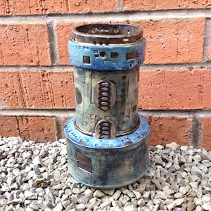 May include: A blue and brown ceramic vase with a geometric design. The vase has a cylindrical shape and a wide base. It is decorated with a pattern of circles, squares, and lines.