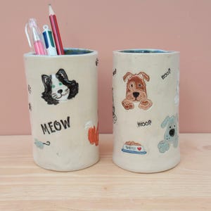 May include: Two ceramic pencil holders, one with a cat design and the word "MEOW" and the other with a dog design and the word "WOOF".