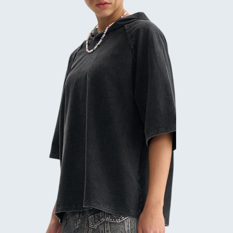 May include: A black short-sleeve hoodie with a washed, vintage look. The hoodie has a drawstring hood and a relaxed fit. The fabric appears soft and slightly faded. The garment is a solid color, suitable for casual wear.