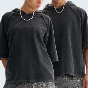 May include: Two people wearing matching charcoal gray hooded t-shirts with short sleeves. The shirts have a washed, vintage look. Each person is wearing a necklace. The background is a plain white.