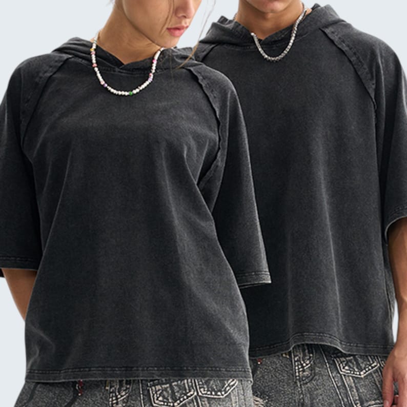 May include: Two people wearing matching charcoal gray hooded t-shirts with short sleeves. The shirts have a washed, vintage look. Each person is wearing a necklace. The background is a plain white.