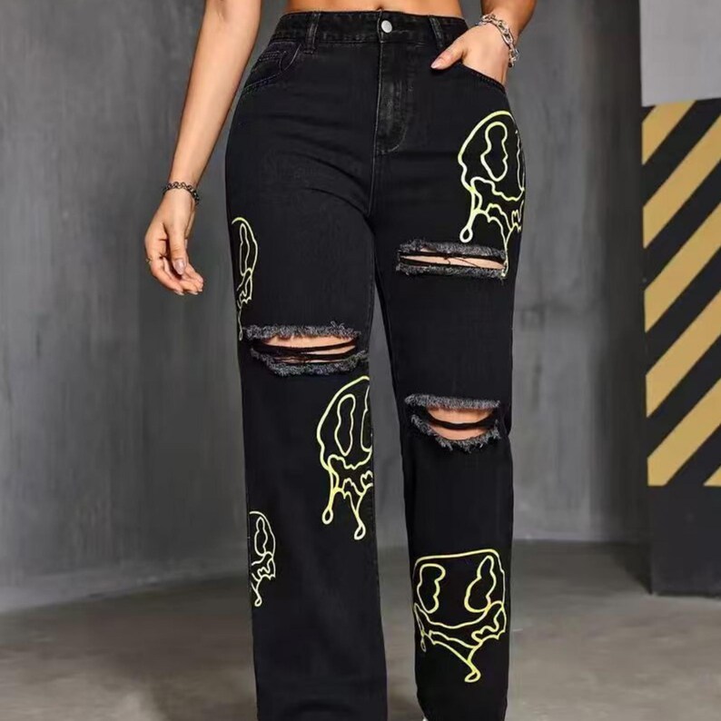 Pu&ograve; includere: Jeans in denim nero con dettagli strappati e disegni di faccine gialle. I jeans hanno una vestibilit&agrave; a gamba dritta e presentano ginocchia strappate. Una rivisitazione moderna di uno stile classico.