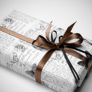 May include: A wrapped gift with vintage-style paper featuring script and butterfly illustrations. The gift is tied with a brown satin ribbon and a black ribbon, creating a decorative bow. The overall aesthetic is elegant and classic.