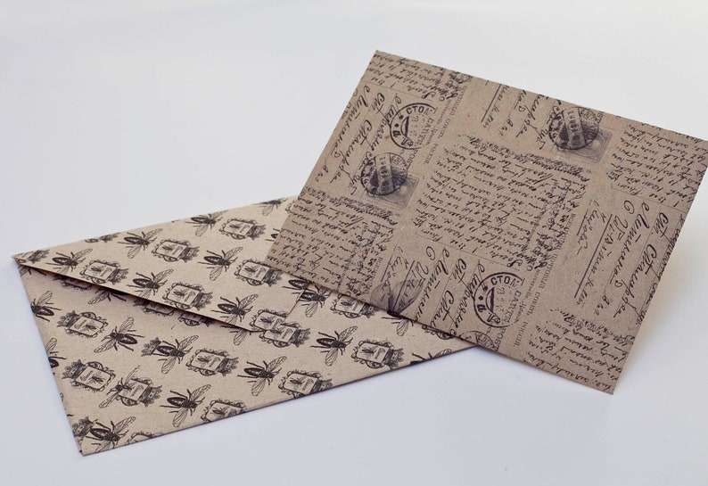 May include: Two decorative envelopes. One envelope features a repeating pattern of black insects and postage stamp designs on a tan background. The other envelope has a vintage script and postage stamp design on a tan background.