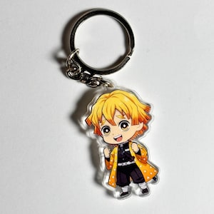 Könnte beinhalten: Ein klarer Acryl-Schlüsselanhänger mit einem Anime-Charakter im Chibi-Stil mit gelben und orangefarbenen Haaren, der ein gelbes und schwarzes Outfit trägt. Der Schlüsselanhänger hat einen silbernen Metallring zur Befestigung.
