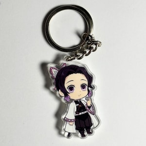 Könnte beinhalten: Ein klarer Acryl-Schlüsselanhänger mit einem Anime-Charakter im Chibi-Stil mit lila Haaren und Augen, der einen weißen Mantel und ein schwarzes Outfit trägt. Der Schlüsselanhänger hat einen silbernen Metallring und eine Kette.