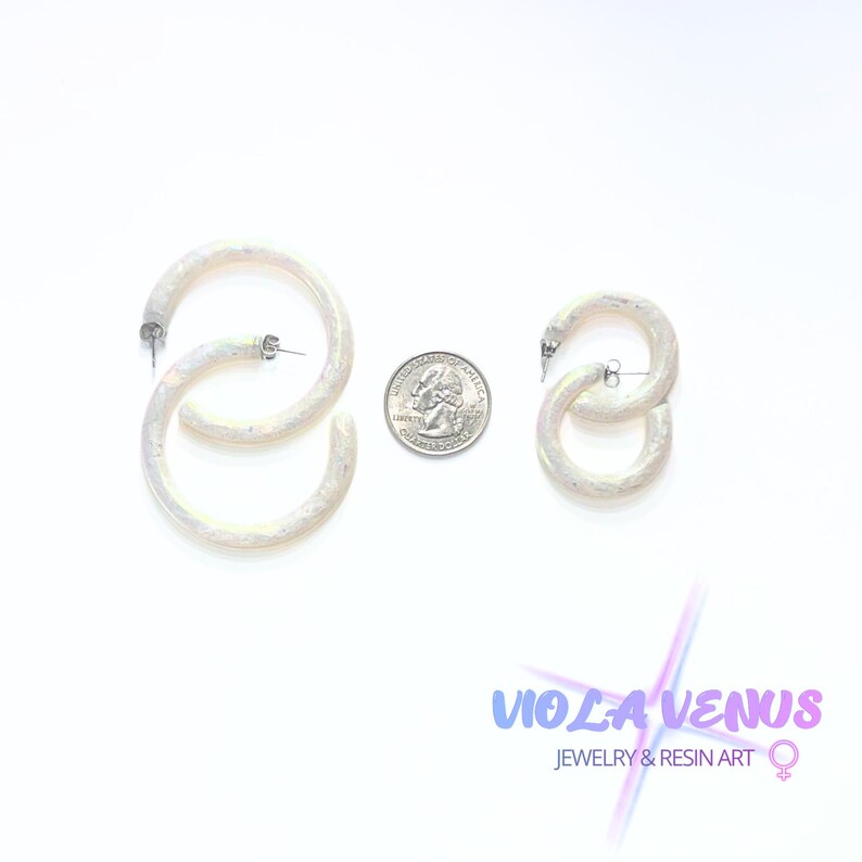 May include: Two pairs of iridescent white hoop earrings with a textured finish, displayed alongside a United States quarter coin for scale. The text Viola Venus Jewelry & Resin Art is visible in the lower right corner with a female symbol icon.