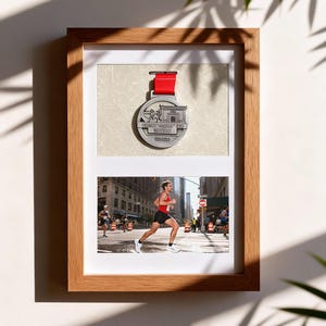 Könnte beinhalten: Ein gerahmtes Display mit einer Laufmedaille und einem Foto eines Marathonläufers. Die Medaille hat ein rotes Band. Das Foto zeigt einen Läufer in einer Stadt. Der Rahmen ist aus hellem Holz, sportliches Thema.