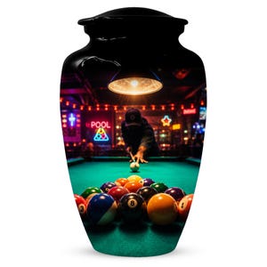 May include: A black cremation urn featuring a high-resolution wrap-around print of a pool hall scene. The image displays a person aiming a cue stick at a white cue ball on a green felt table, surrounded by colourful billiard balls and neon signs.