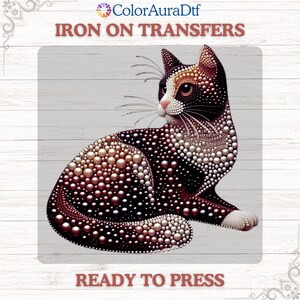May include: An iron-on transfer featuring a stylized cat design. The cat is black and white with a pattern of small, pearl-like dots. The text "IRON ON TRANSFERS" and "READY TO PRESS" are displayed.