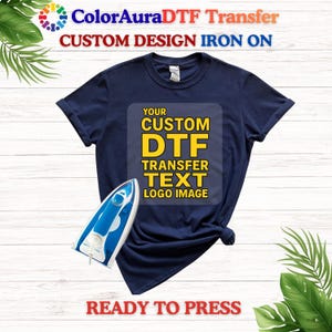 May include: Navy blue t-shirt with a custom DTF transfer design area. The shirt has the text "YOUR CUSTOM DTF TRANSFER TEXT LOGO IMAGE" printed on it. A blue and white iron is placed on the shirt. The text "READY TO PRESS" is at the bottom.