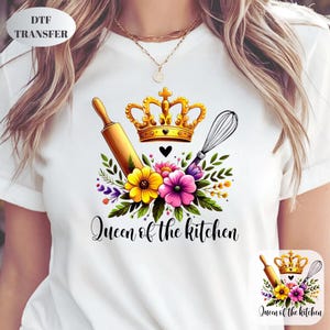 May include: White t-shirt featuring a colorful design with a gold crown, rolling pin, and whisk. The design includes yellow and pink flowers, green leaves, and the text "Queen of the kitchen". A DTF transfer is visible in the upper left corner.
