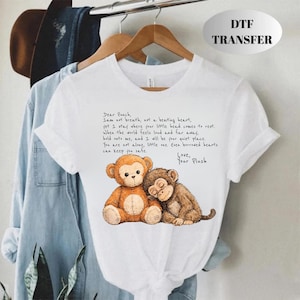 May include: White t-shirt featuring a watercolor illustration of two plush monkeys, one brown and one tan, with the text "Dear Punch, I am not breath, not a beating heart..." and "Love, Your Plush."