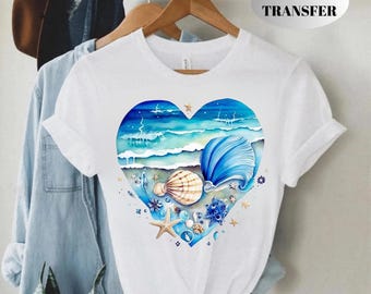 Op de afbeelding: Wit T-shirt met een hartvormig aquarel strandontwerp. Het ontwerp toont blauwe oceaangolven, schelpen en een zeester. De tekst "DTF TRANSFER" is rechtsboven zichtbaar.