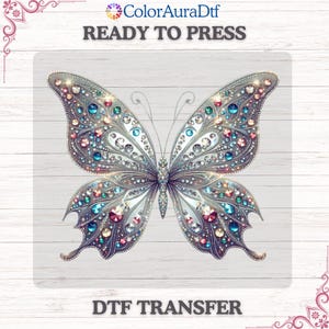May include: A detailed butterfly design with silver and jewel-toned accents. The butterfly is adorned with sparkling gems in shades of blue, pink, and clear. The words "READY TO PRESS" and "DTF TRANSFER" are printed on the image.