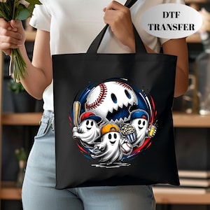 May include: A black tote bag featuring a graphic of three white ghosts wearing baseball caps. One ghost holds a wooden bat, another holds a bucket of popcorn, and the third holds a baseball. A large baseball with a jagged mouth sits behind them.