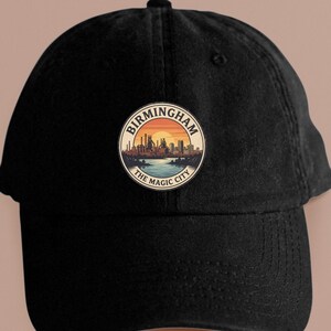 May include: Black baseball cap with a circular patch featuring a cityscape silhouette against a sunset. The patch reads "Birmingham" and "The Magic City" in a circular design. The cap has a curved brim and an adjustable strap.