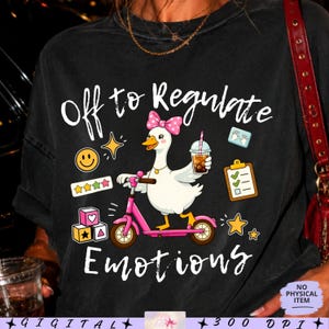 Könnte beinhalten: Ein schwarzes T-Shirt mit einer weißen Gans, die eine rosa gepunktete Schleife trägt, auf einem rosa Roller fährt und ein Getränk hält. Der Text lautet Off to Regulate Emotions. Grafiken zeigen einen Smiley, Sterne, Bauklötze, eine Liste und Handabdrücke.