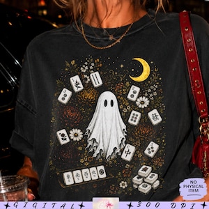 May include: A black t-shirt featuring a central white ghost illustration surrounded by scattered mahjong tiles, small white flowers, and a yellow crescent moon. The graphic includes various mahjong tiles with symbols and characters arranged around the ghost.