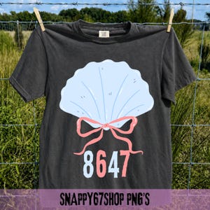 Könnte beinhalten: Ein dunkelgraues T-Shirt mit einem hellblauen Muscheldesign, einer rosa Schleife und der Nummer 8647 in Weiß und Rosa. Das T-Shirt hängt an einer Wäscheleine. Der Text "SNAPPY67SHOP PNG'S" steht unten.