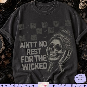 Könnte beinhalten: Ein anthrazitfarbenes Kurzarm-T-Shirt mit einem abgenutzten Schachbrettmuster im oberen Bereich. Die Grafik zeigt einen menschlichen Schädel mit hochgestecktem Haar, skelettierte Hände, die das Gesicht einrahmen, und den Text AINT'T NO REST FOR THE WICKED.