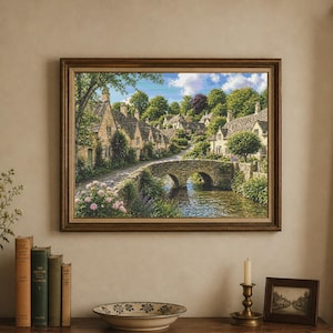 May include: A framed landscape painting depicts a quaint village with stone houses, a bridge over a river, and lush greenery. The artwork is displayed above a wooden surface with books, a vase of flowers, and decorative items.
