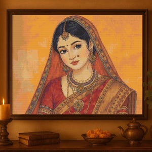 Puede incluir: Retrato enmarcado de una mujer con vestimenta tradicional india, con un sari rojo y joyas ornamentadas. La obra de arte está ambientada sobre un fondo cálido y dorado. Una vela encendida, libros y un cuenco decorativo están sobre una superficie de madera.