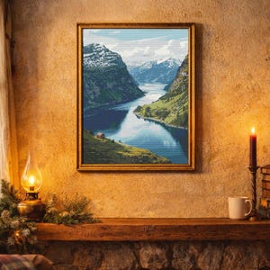 Può includere: Un'opera d'arte incorniciata raffigurante una serena scena di fiordo con montagne innevate, un lago blu calmo e verdi colline. L'opera è esposta sopra un camino in pietra, con una candela accesa e una lampada a olio vintage.