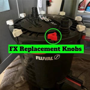Puede incluir: Filtro de repuesto Fluval FX negro con el texto "FX Replacement Knobs". El filtro tiene un cuerpo negro con una parte superior negra y perillas rojas. El filtro tiene perillas blancas en la parte superior.