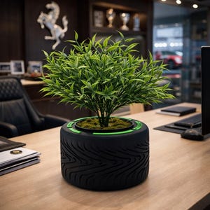 Pode incluir: Um vaso preto em forma de pneu com uma borda verde e uma planta verde. O vaso tem um design de banda de rodagem de pneu texturizado. A planta tem muitas folhas verdes e é plantada em um leito de musgo.