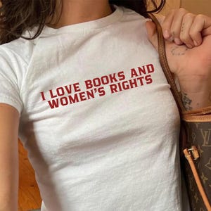 White baby tee ''I LOVE BOOKS AND WOMEN'S RIGHTS'' text is written in red on it.