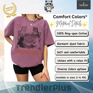 Może przedstawiać: Malinowy t-shirt z kr&oacute;tkim rękawem z grafiką przedstawiającą cztery koty grające w mahjonga przy stole. Projekt zawiera napis MEOWJONG oraz chińskie znaki w rogach. Koszulka wykonana jest w 100% z bawełny ring-spun o luźnym kroju.