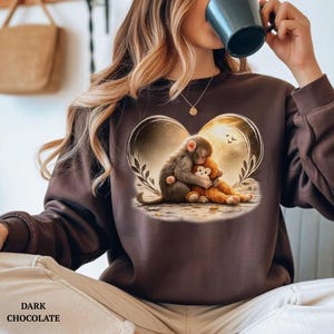 Dark chocolate-colored sweatshirt featuring a heart-shaped design with a monkey hugging a teddy bear. The design includes a background of a sunset and foliage.