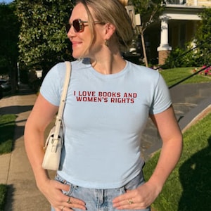 Light Blue baby tee ''I LOVE BOOKS AND WOMEN'S RIGHTS'' text is written in red on it.