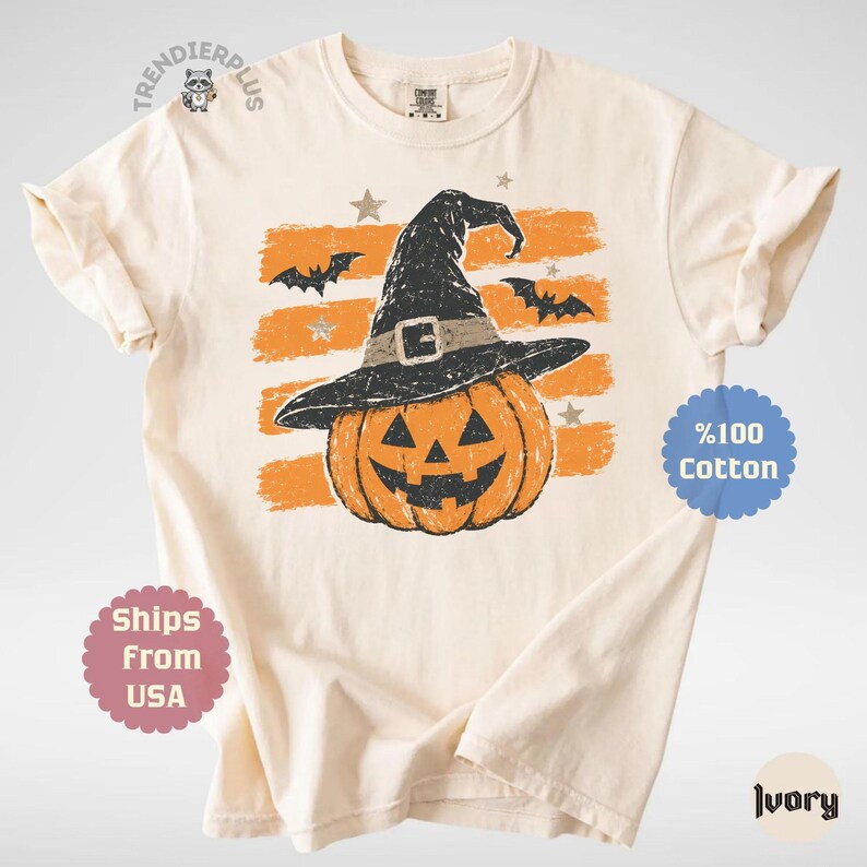 Puede incluir: Una camiseta de manga corta color marfil con un gr&aacute;fico de una calabaza de Halloween que lleva un sombrero de bruja negro. El dise&ntilde;o incluye trazos de pincel horizontales de color naranja, murci&eacute;lagos negros y peque&ntilde;as estrellas.