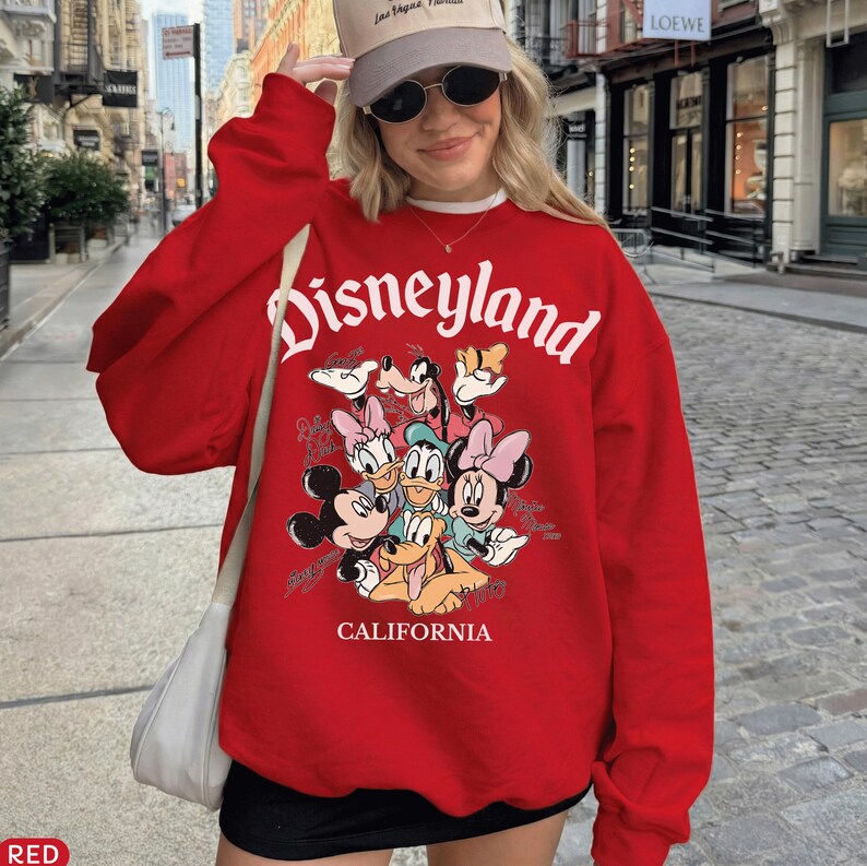 May include: A red Disneyland sweatshirt featuring a graphic of Mickey Mouse, Minnie Mouse, Donald Duck, Daisy Duck, Goofy, and Pluto. The word "Disneyland" is arched across the top, with "CALIFORNIA" below the characters.