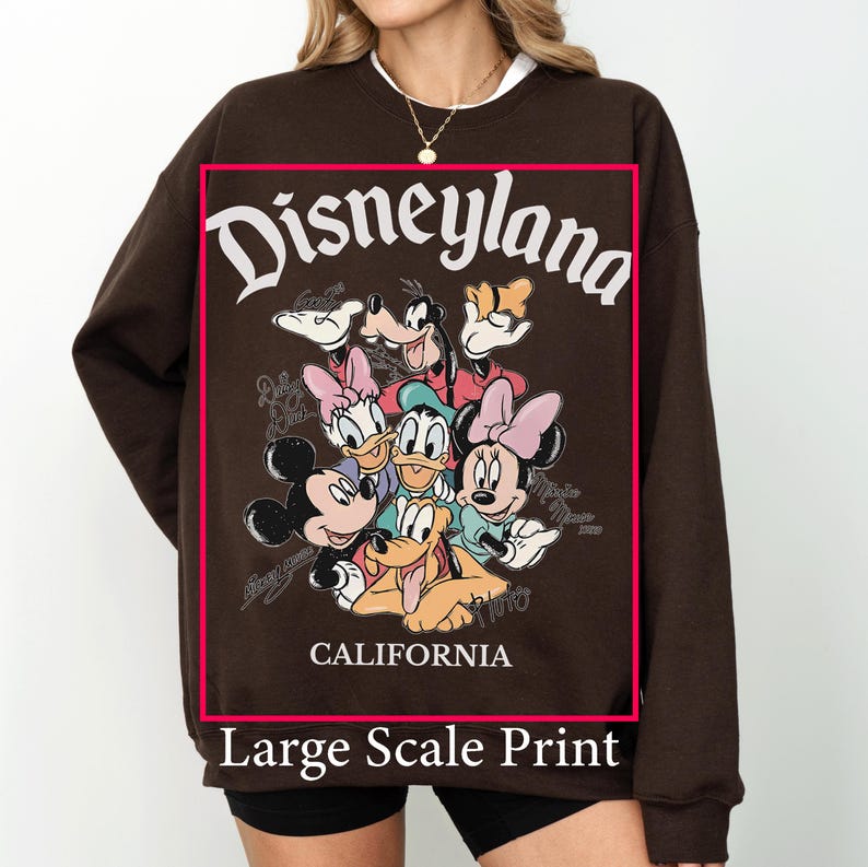 May include: A brown sweatshirt featuring a large graphic print of Disneyland characters, including Mickey Mouse, Minnie Mouse, Donald Duck, and Goofy. The word "Disneyland" is arched across the top, with "California" below. The words "Large Scale Print" are at the bottom.