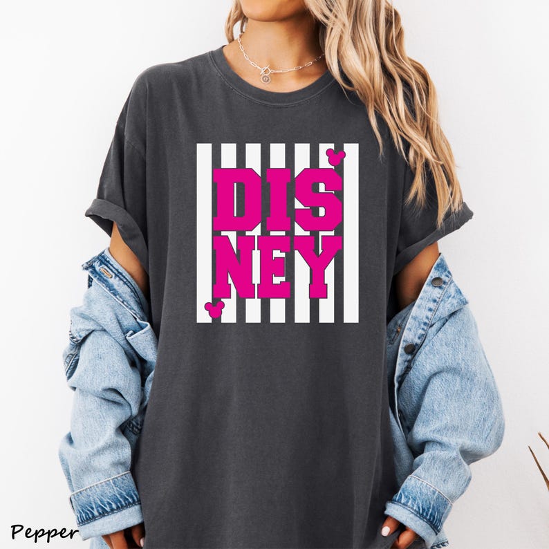 May include: Dark gray t-shirt with a pink "DISNEY" graphic in a white striped rectangle. The word "Pepper" is printed in the bottom left corner. The shirt has short sleeves and a relaxed fit.