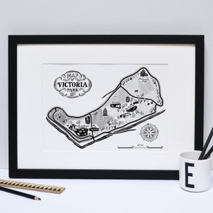 May include: Black and white map print of Victoria Park, 1835, framed in a black frame. The map includes detailed illustrations of park features, a compass rose, and the text "Map of Victoria Park 1835". A ruler and pencil are on the left.