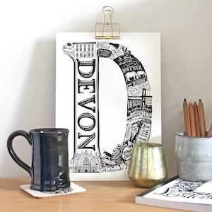 Puede incluir: Ilustración en blanco y negro de la letra D, llena de lugares emblemáticos y puntos de interés de Devon, Inglaterra. La palabra "DEVON" está escrita verticalmente en el centro de la letra.