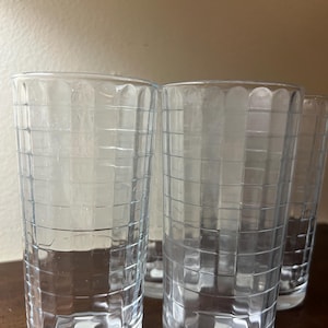 May include: A set of three clear glass tumblers featuring a vertical and horizontal grid pattern etched into the exterior surface. Each cylindrical drinking glass has a smooth rim and a thick, solid base, with a small white sticker on the bottom.
