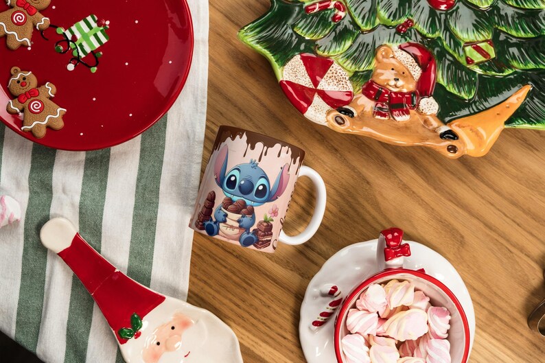 May include: A festive holiday scene with a red plate featuring gingerbread men and a gift, a Stitch mug, and a Santa-shaped plate. A Christmas tree-shaped plate and a bowl of marshmallows complete the arrangement. The items are on a wooden surface.