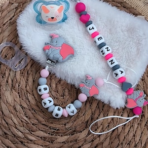 Peut inclure: Ensemble de sucettes pour bébé comprenant une sucette bleue et blanche avec un visage d'animal de dessin animé, un clip de sucette avec le nom "JENNA" épelé en perles blanches et grises, et un clip assorti avec les lettres "BABY".